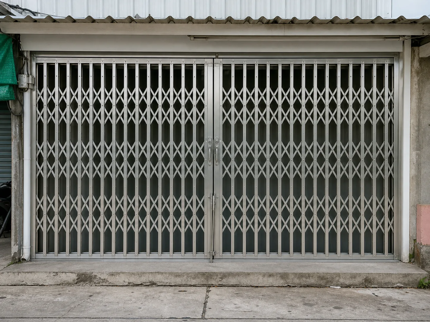 A stainless folding security gate closed across a shopfront, the brushed grain running along the length of each member